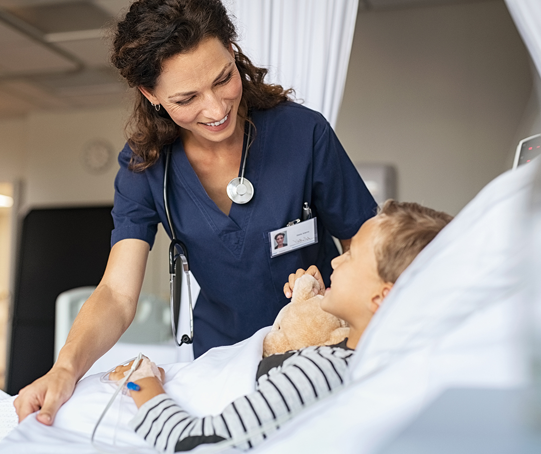 Beautiful kind female nurse taking care of little boy hospitalized in bed. Happy woman nurse tuck the covers back to the young child patient lying on hospital bed. Friendly medical worker talking with kid patient in pediatrics ward at clinic.